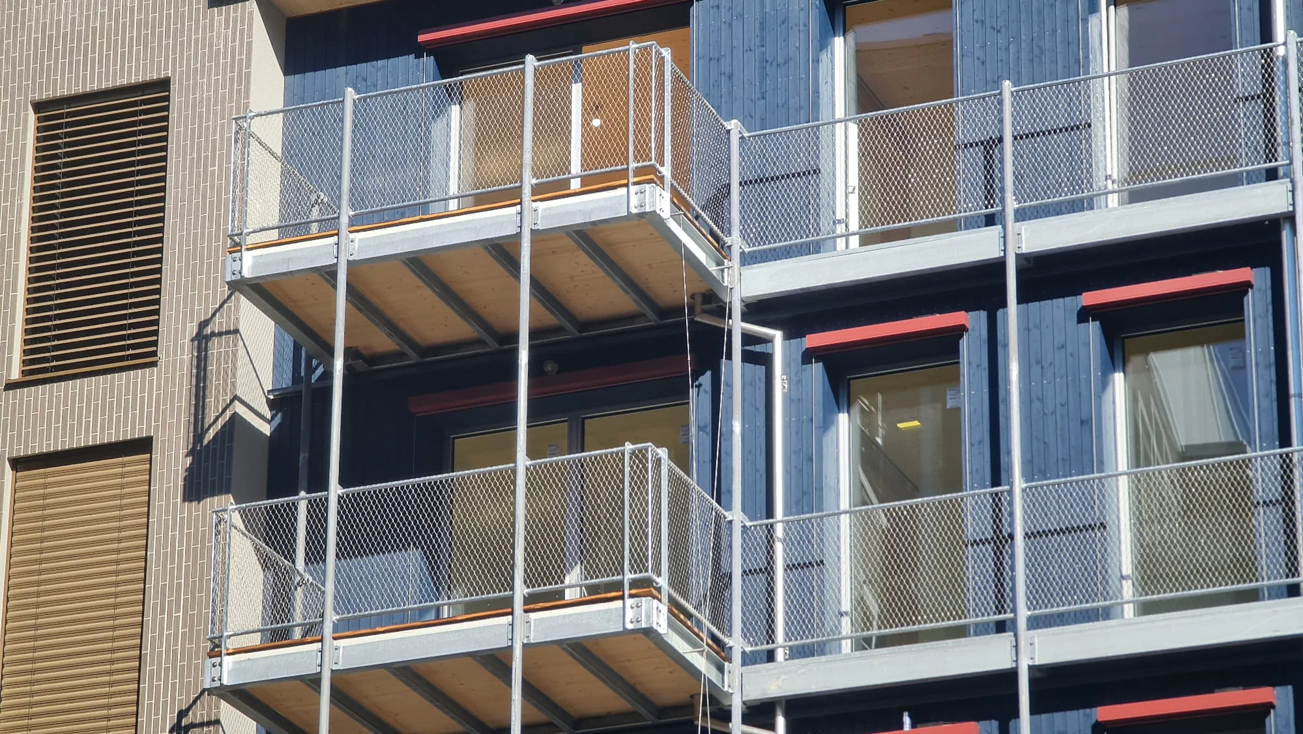 Verzinkte Balkonkonstruktionen mit Netzbrüstung an einem blau verkleideten Wohnbau