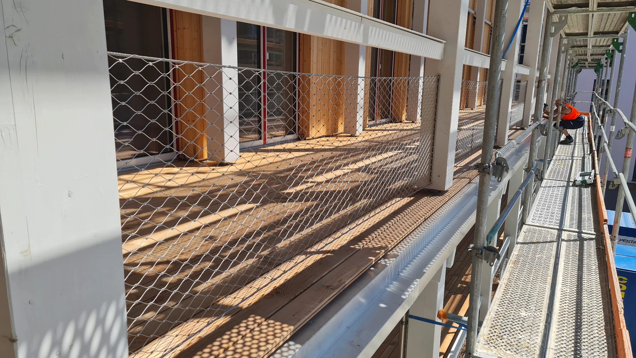 Montage eines langen Balkonlaufs mit Seilnetz-Geländer, Monteur auf dem Gerüst
