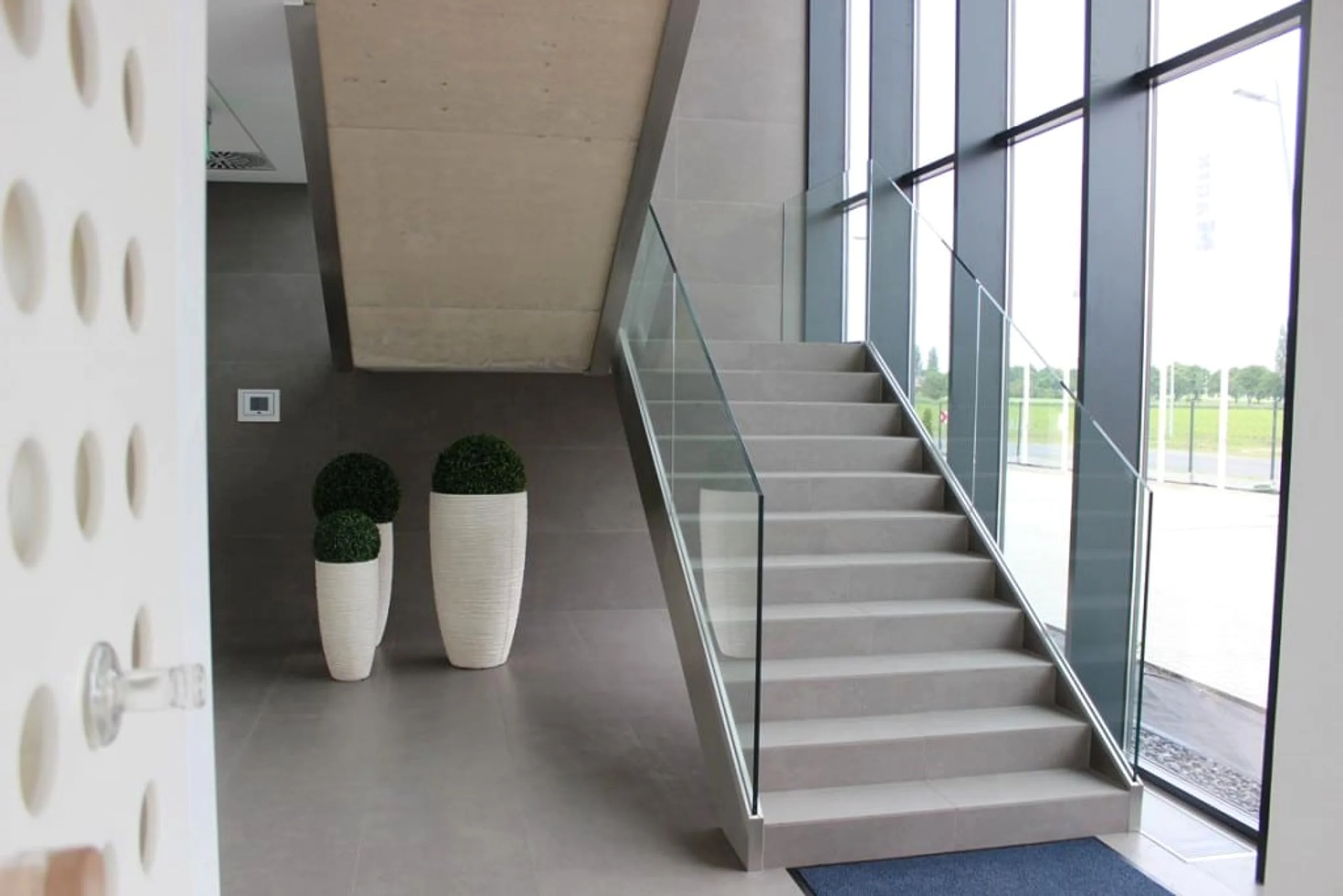 Ganzglas-Balustrade an einer Innentreppe, dahinter eine raumhohe Pfosten-Riegel-Fassade