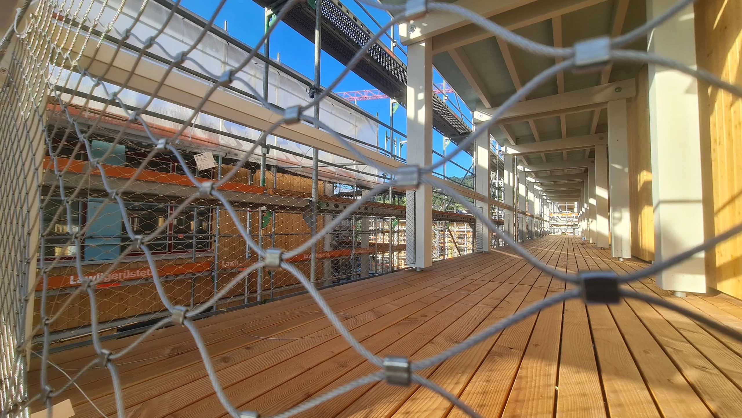 Laubengang mit Holzdeck und Seilnetz-Geländer, Gerüst an der Fassade