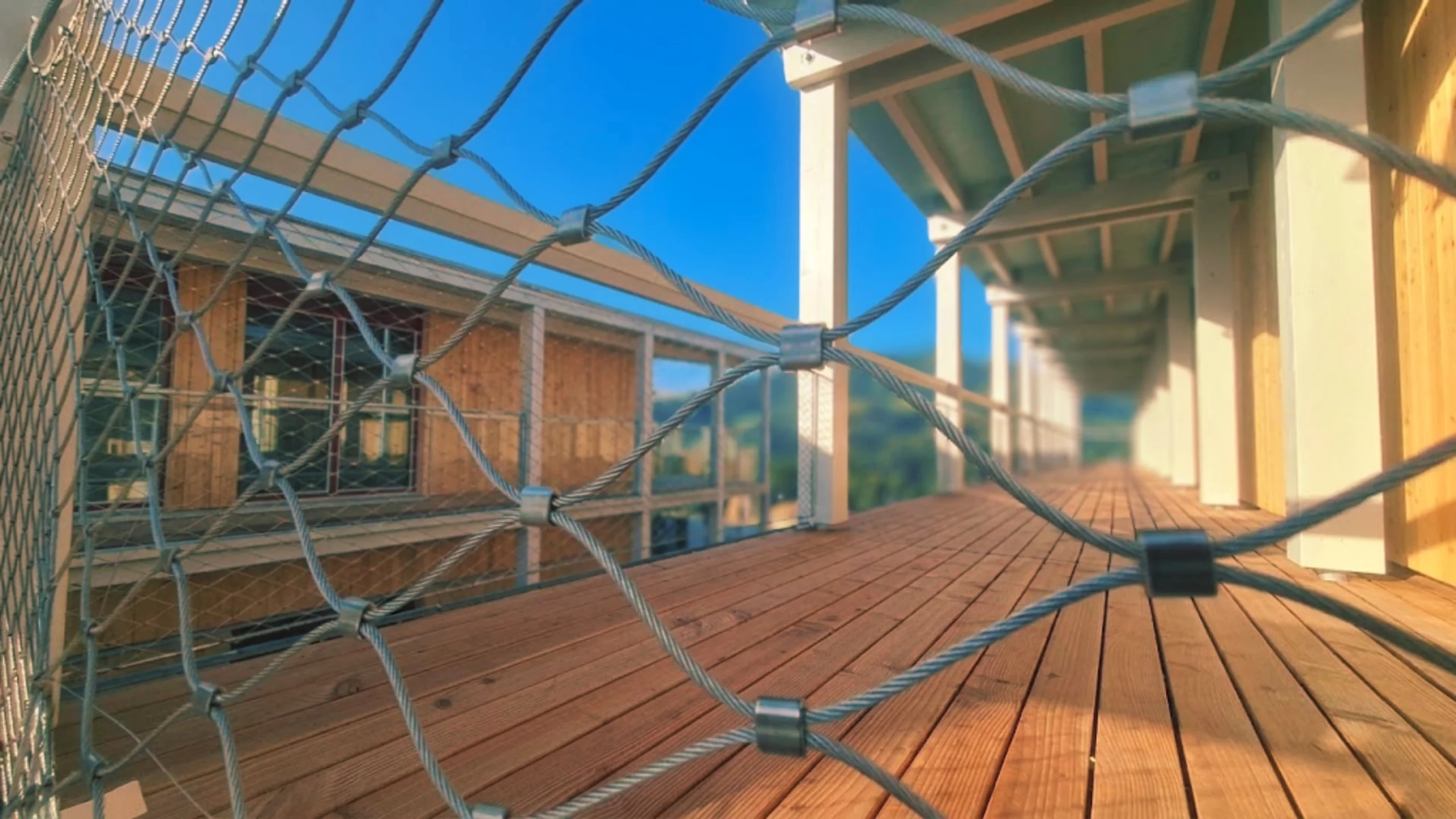 Blick entlang eines Laubengangs mit Holzdeck durch die gespannte Seilnetzbrüstung