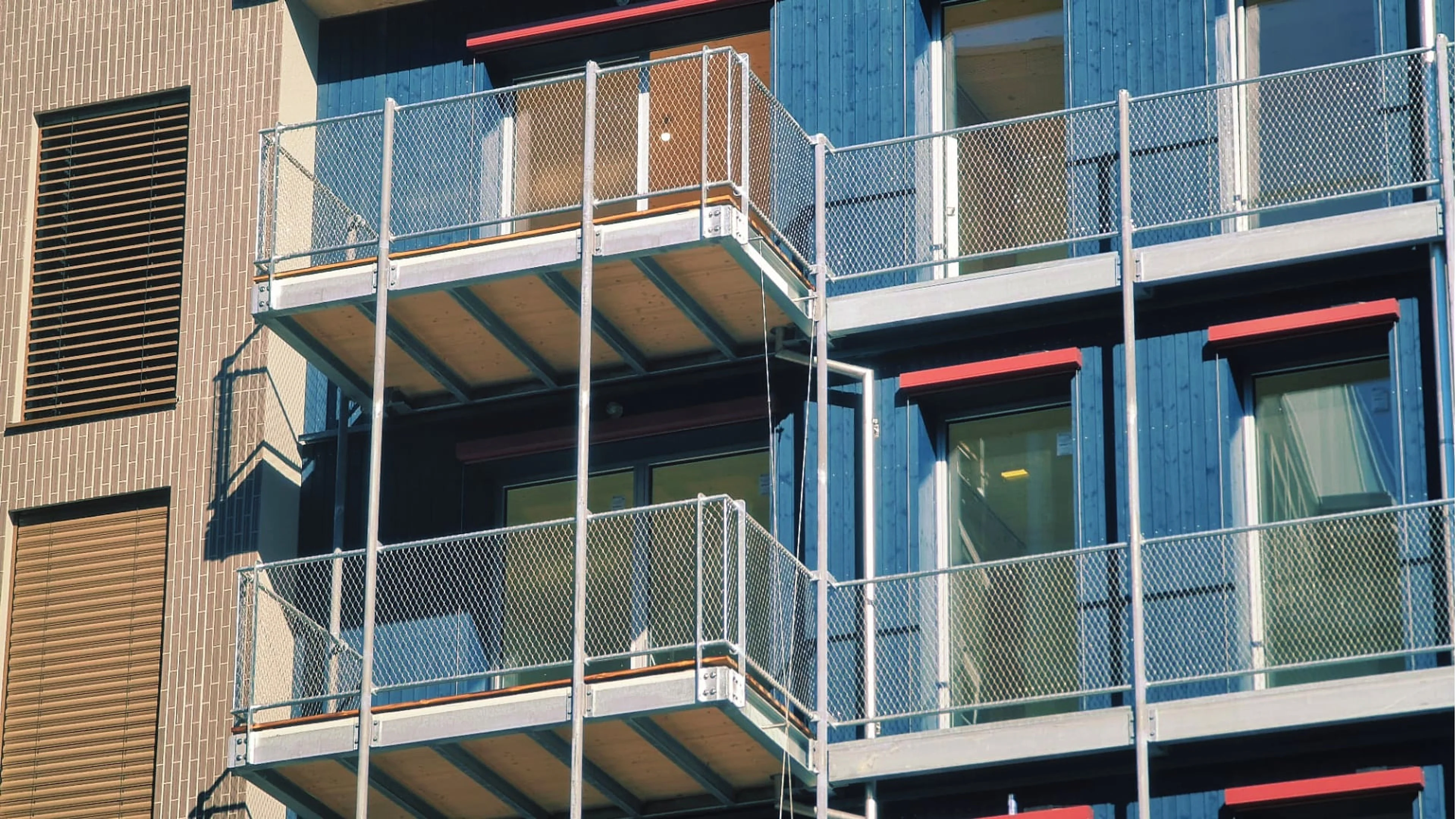 Verzinkte Balkonkonstruktionen mit Netzbrüstung an einer blau verkleideten Holzfassade