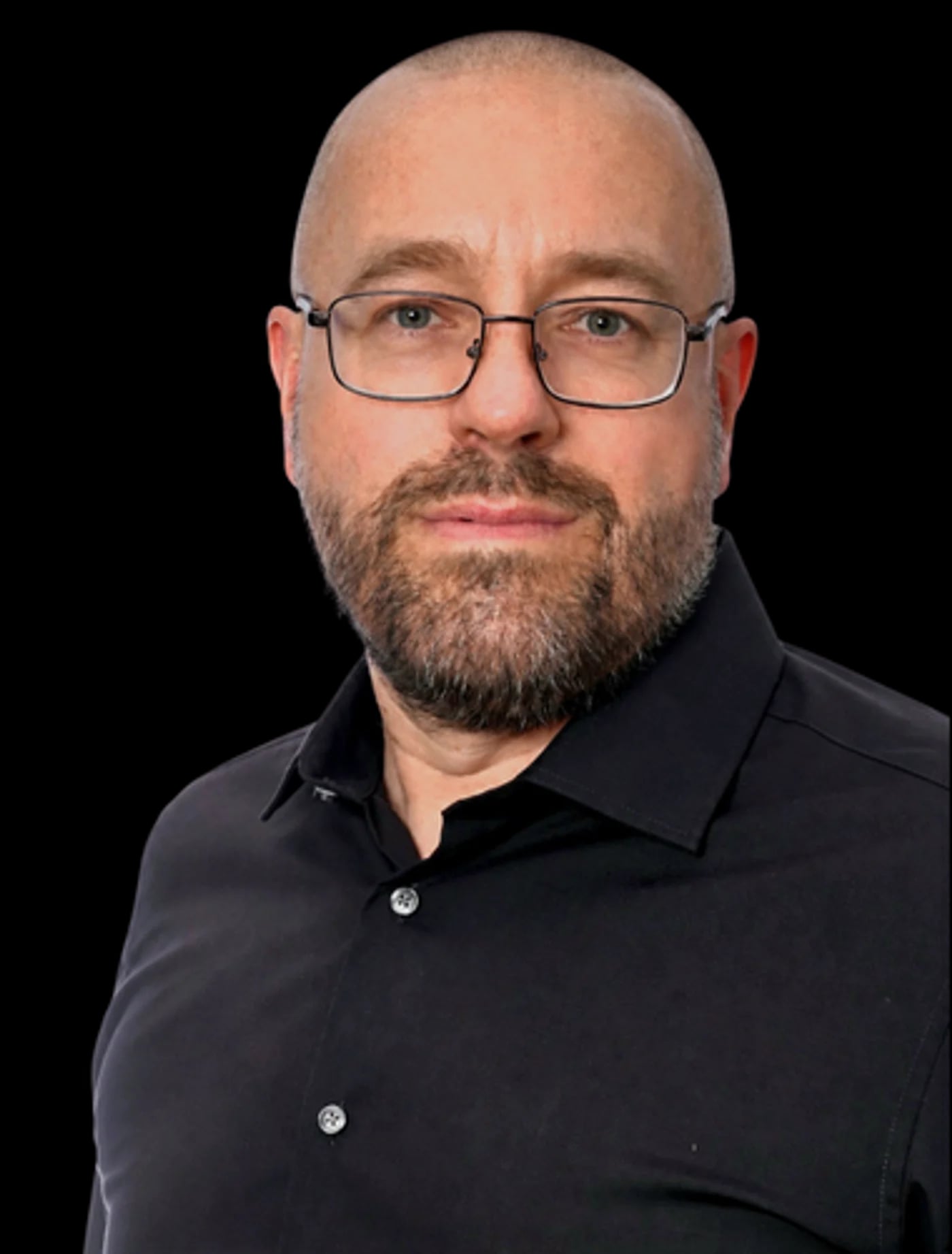 Porträtaufnahme eines Mannes mit Brille und Bart im schwarzen Hemd vor hellem Studiohintergrund